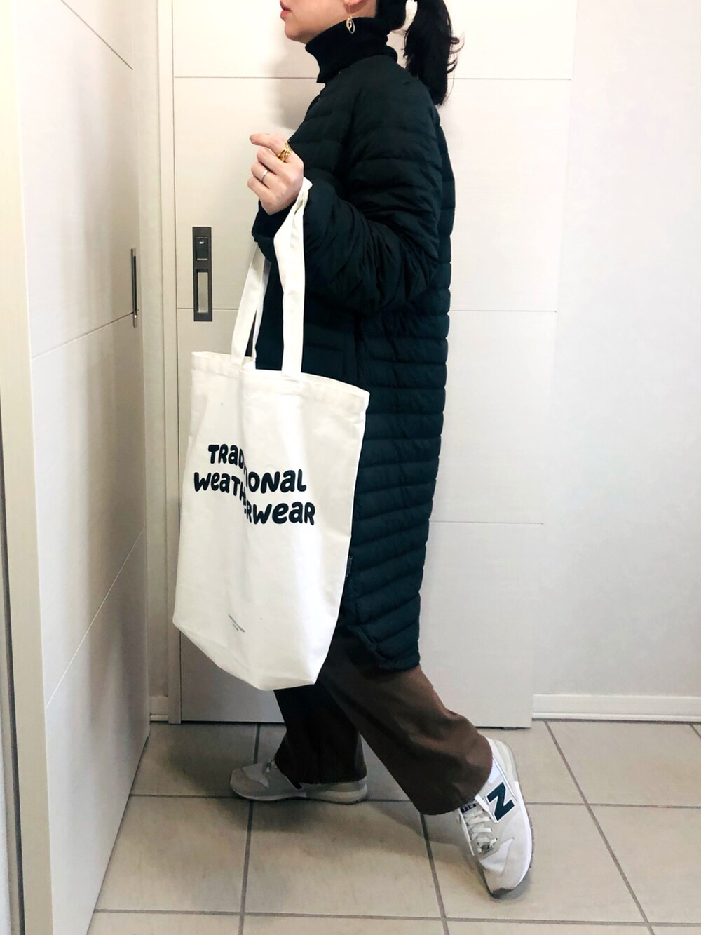ブラック系のダウンジャケット/コート、ブラック系のニット/セーター、ブラウン系のチノパンツを着用したレディースの冬コーディネートの3枚目の写真