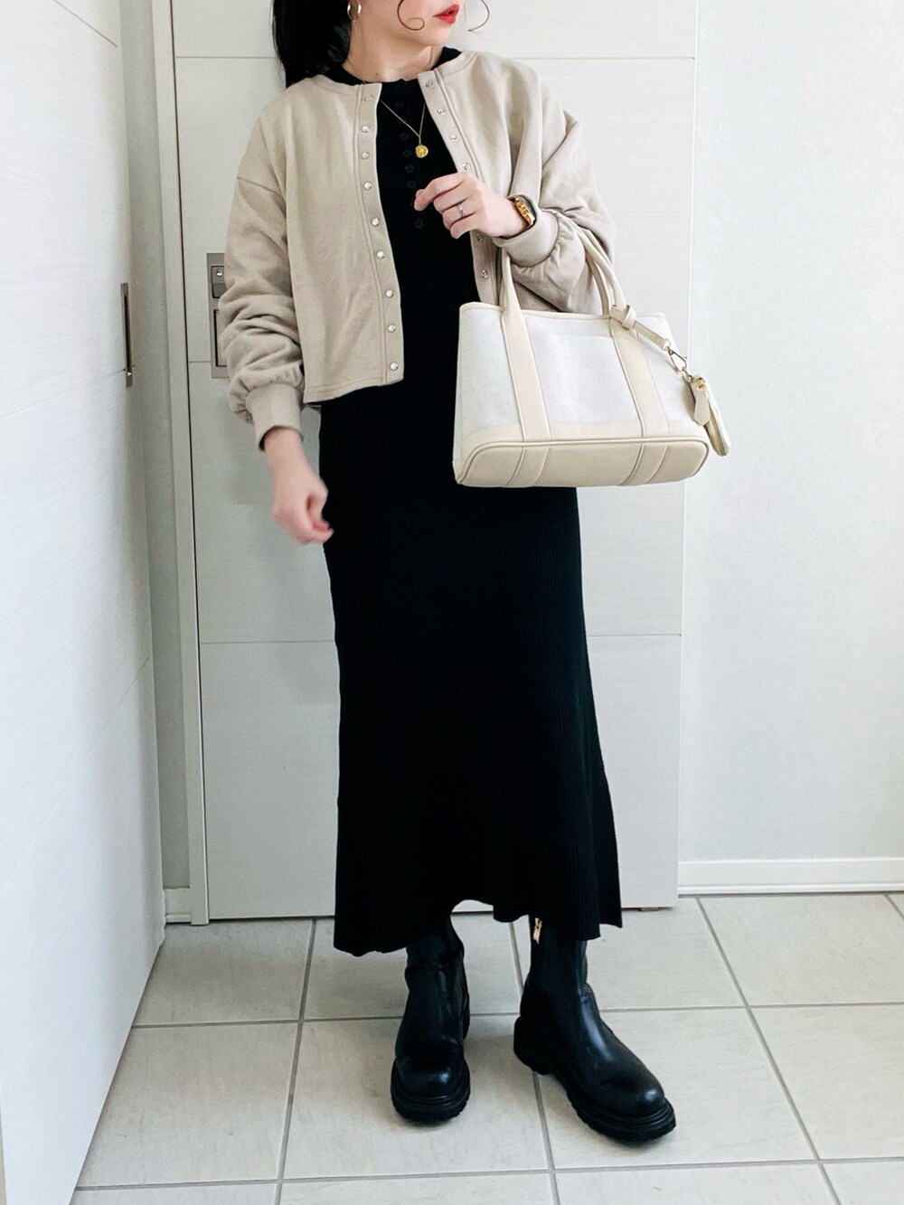 ベージュ系のカーディガン/ボレロ、ブラック系のワンピース、ブラック系のブーツを着用したレディースの冬コーディネートの2枚目の写真