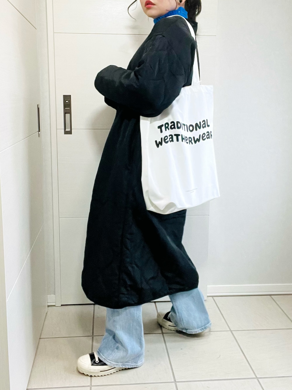 ブラック系のノーカラーコート、ブルー系のニット/セーター、ブルー系のデニムパンツを着用したレディースの秋コーディネートの5枚目の写真