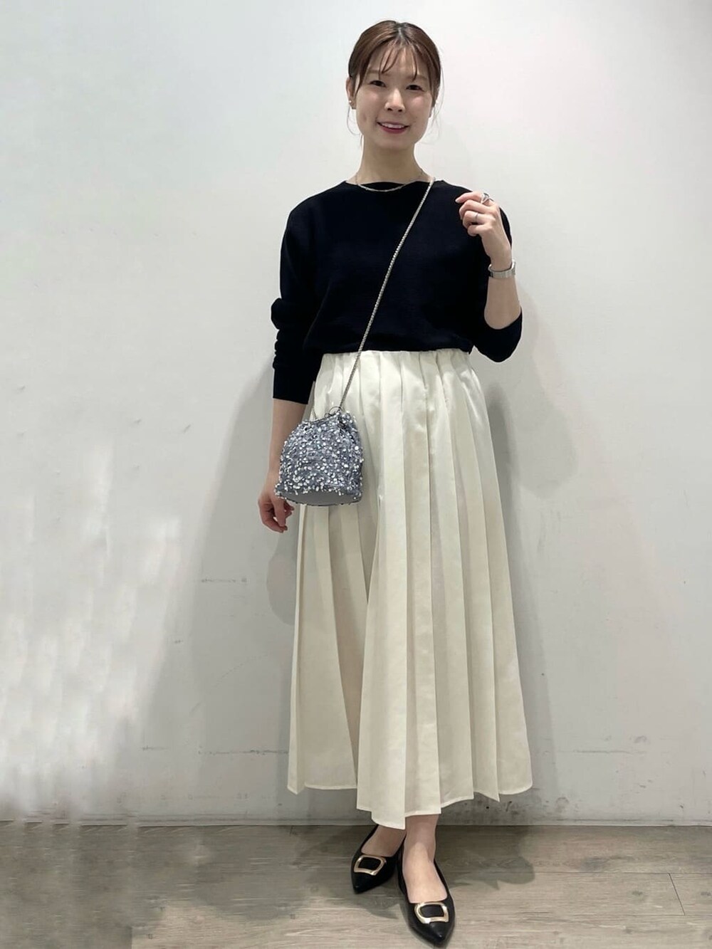 グレー系のショルダーバッグ、ブラック系のパンプス、ホワイト系のスカートを着用したレディースの春コーディネートの2枚目の写真