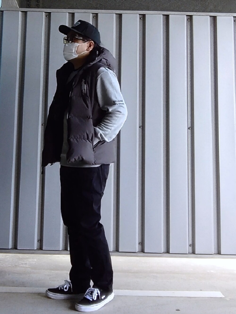 ブラック系のスニーカー、ブラック系のデニムパンツ、グレー系のダウンベストを着用したメンズの春コーディネートの3枚目の写真