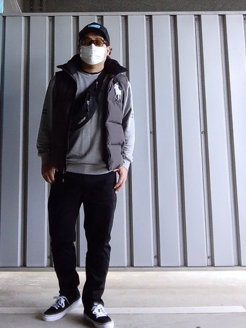 ブラック系のスニーカー、ブラック系のデニムパンツ、グレー系のダウンベストを着用したメンズの春コーディネートの4枚目の写真