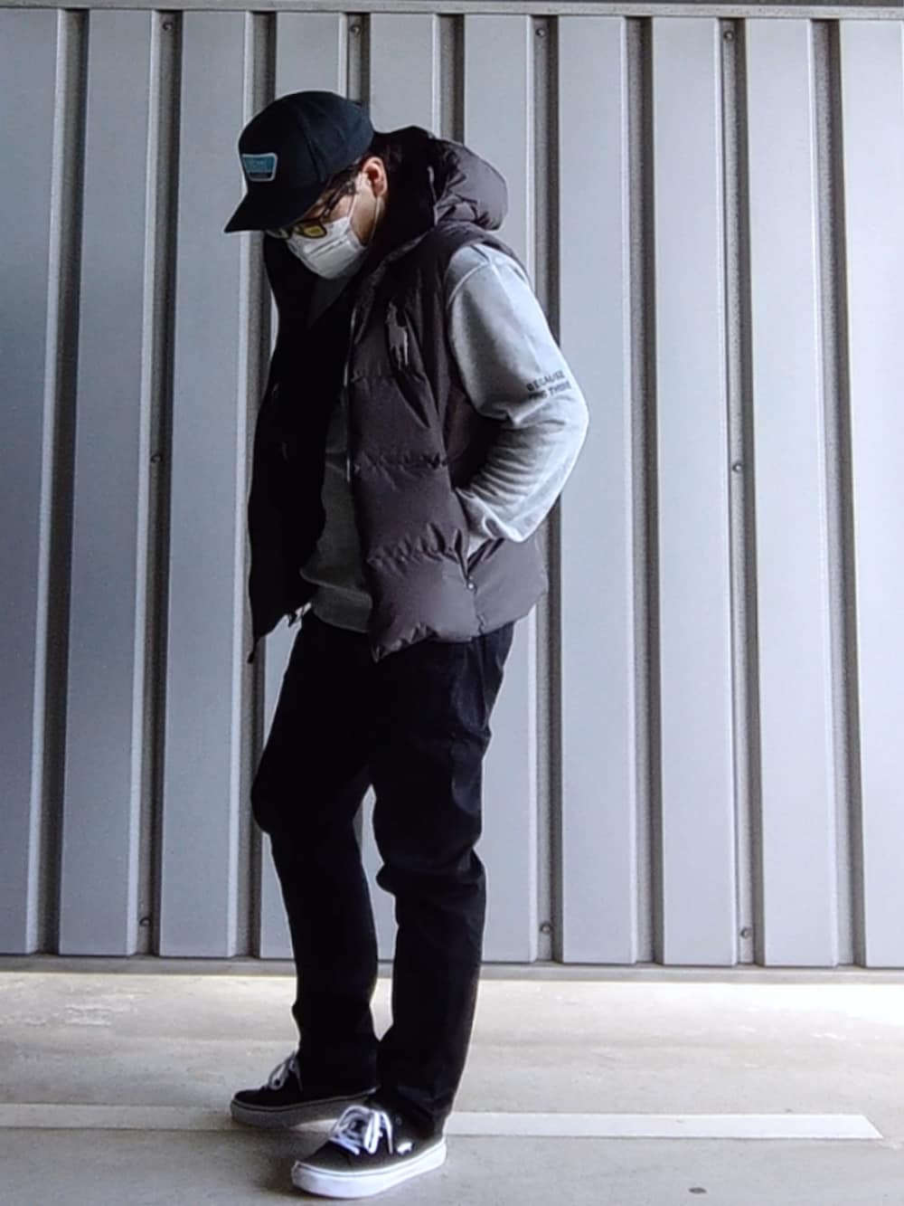 ブラック系のスニーカー、ブラック系のデニムパンツ、グレー系のダウンベストを着用したメンズの春コーディネートの2枚目の写真