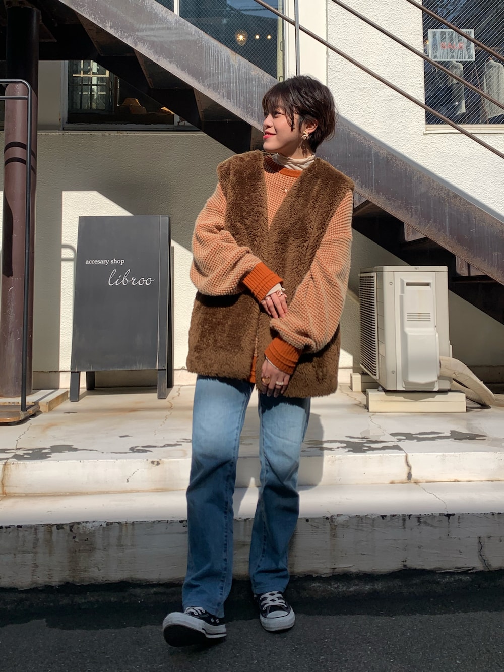 ブラウン系のその他アウター、オレンジ系のニット/セーター、ブルー系のデニムパンツを着用したレディースの冬コーディネートの2枚目の写真