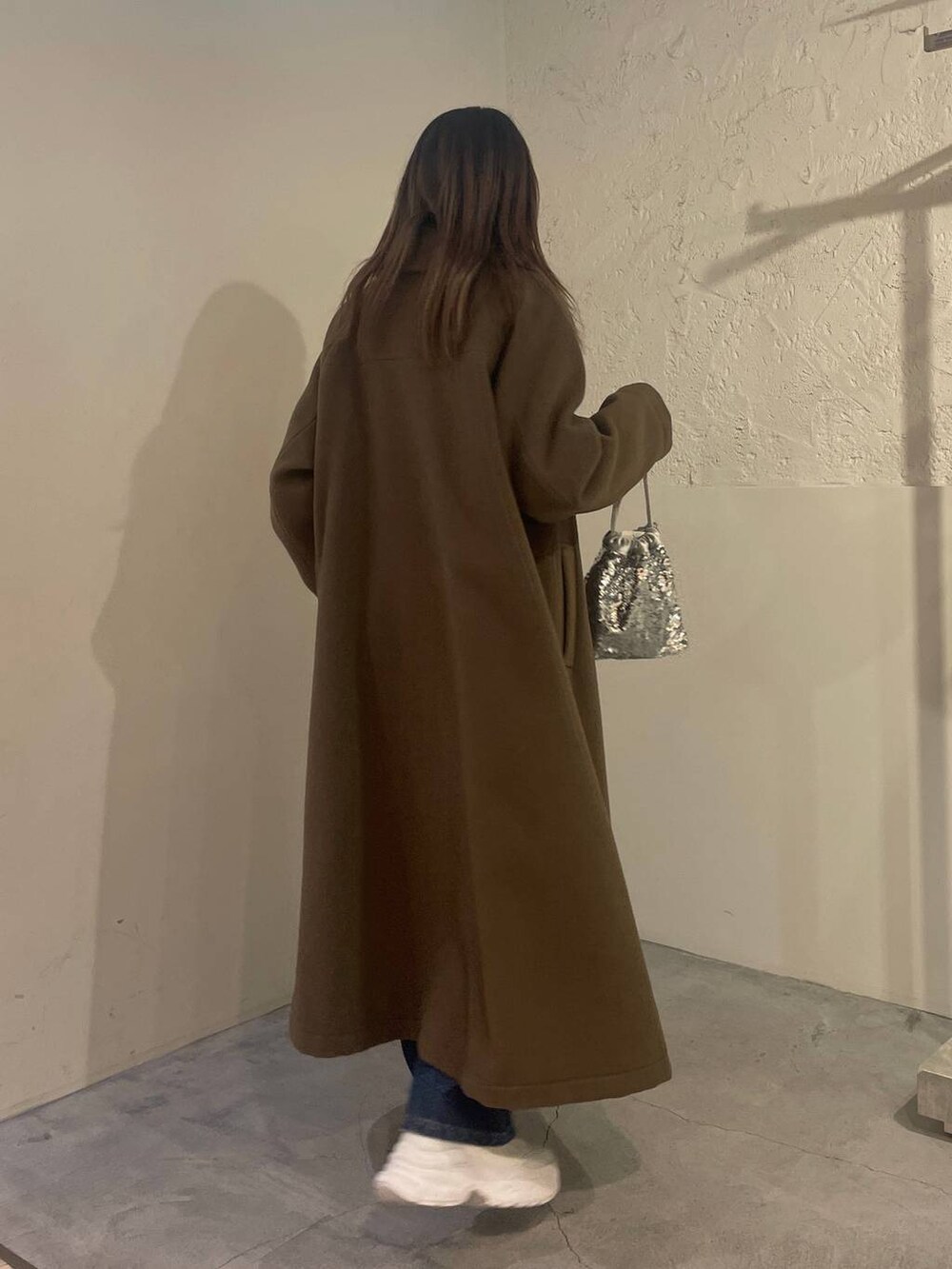 ブラウン系のノーカラーコート、ブルー系のデニムパンツ、シルバー系のハンドバッグを着用したレディースの冬コーディネートの3枚目の写真