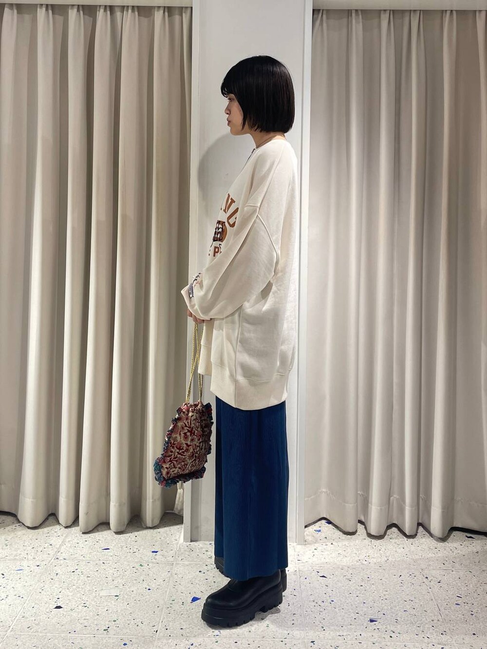 ブルー系のスカート、ホワイト系のハンドバッグ、ブラック系のブーツを着用したレディースの秋コーディネートの4枚目の写真