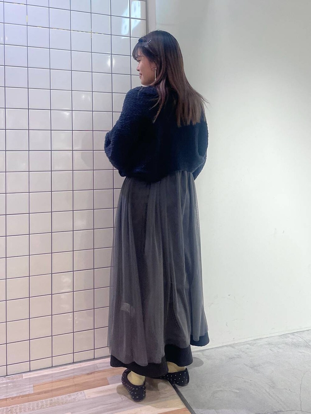 グレー系のワンピース、ホワイト系のショルダーバッグ、ブラック系のスカートを着用したレディースの冬コーディネートの2枚目の写真