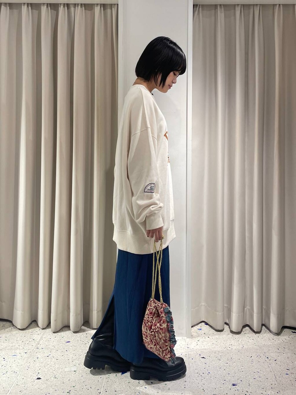 ブルー系のスカート、ホワイト系のハンドバッグ、ブラック系のブーツを着用したレディースの秋コーディネートの2枚目の写真