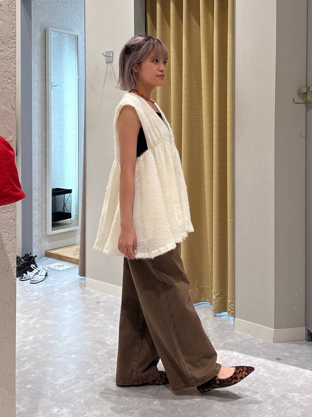 ホワイト系のベスト、ブラウン系のデニムパンツ、ブラック系のキャミソールを着用したレディースの秋コーディネートの3枚目の写真