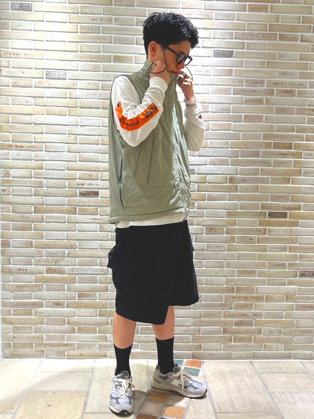 ブラック系のカーゴパンツ、ホワイト系のTシャツ/カットソー、グリーン系のダウンベストを着用したメンズの春コーディネートの2枚目の写真