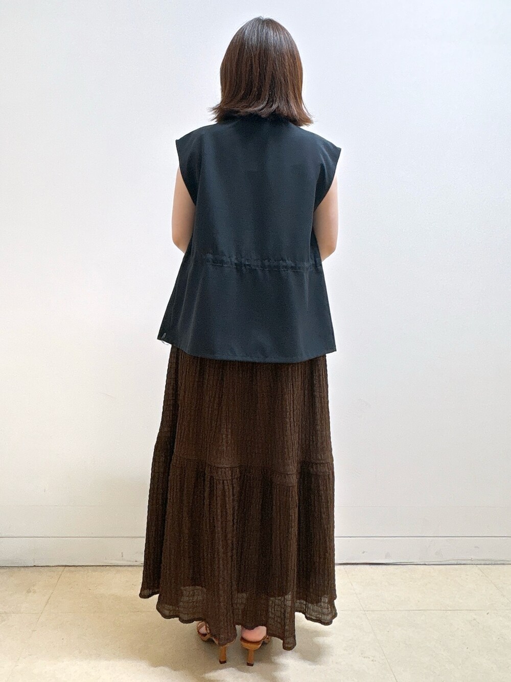 ブルー系のベスト、ブラウン系のスカート、シルバー系のトートバッグを着用したレディースの夏コーディネートの9枚目の写真