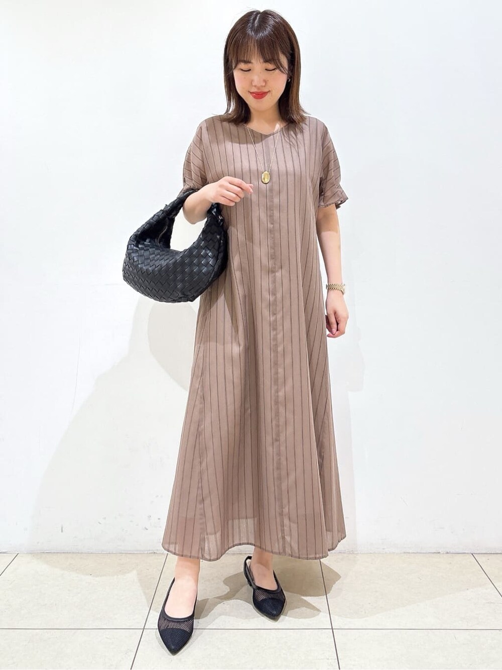 ブラウン系のワンピース、ブラック系のパンプス、ブラック系のハンドバッグを着用したレディースの夏コーディネートの2枚目の写真