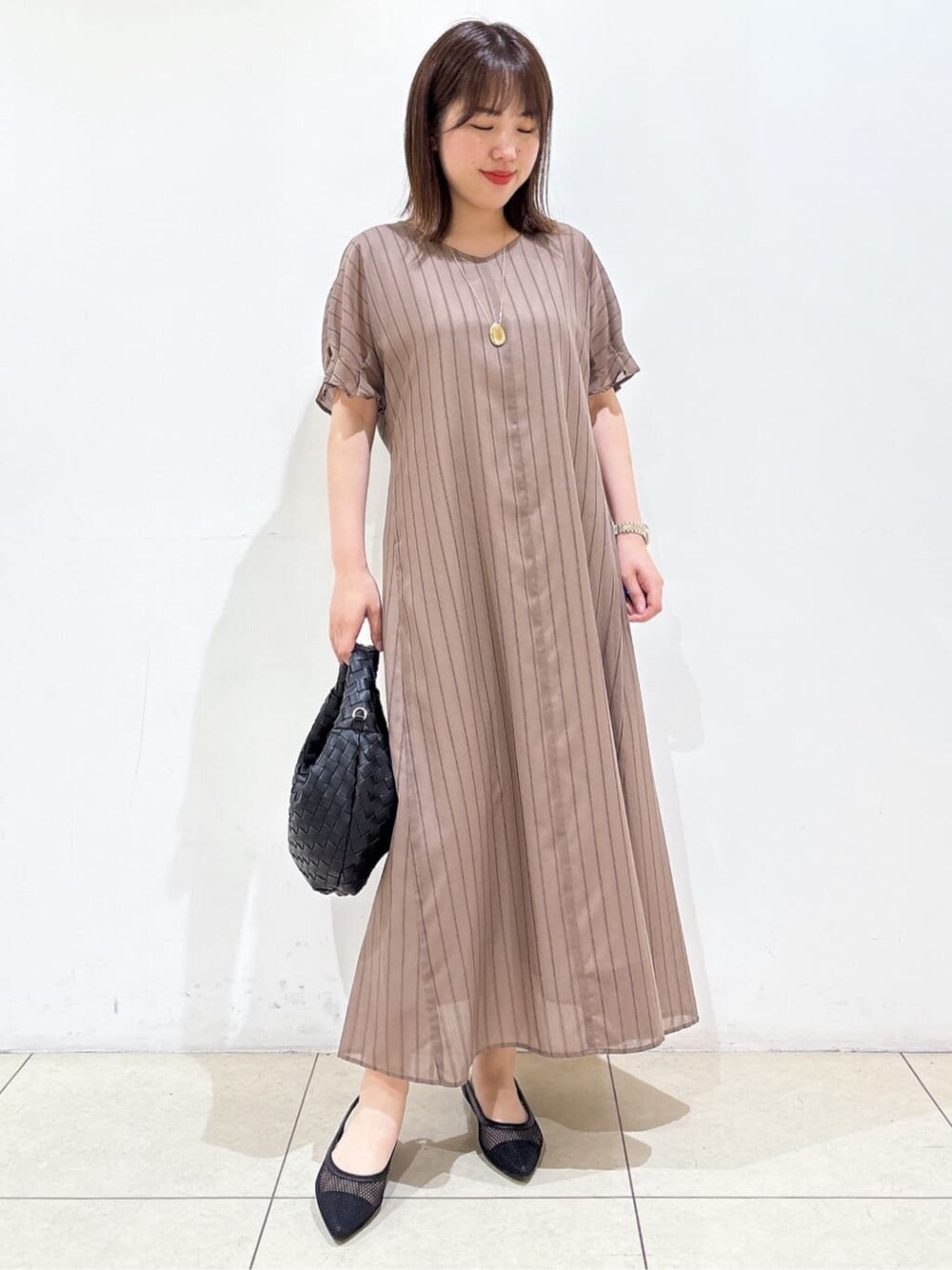 ブラウン系のワンピース、ブラック系のパンプス、ブラック系のハンドバッグを着用したレディースの夏コーディネートの5枚目の写真