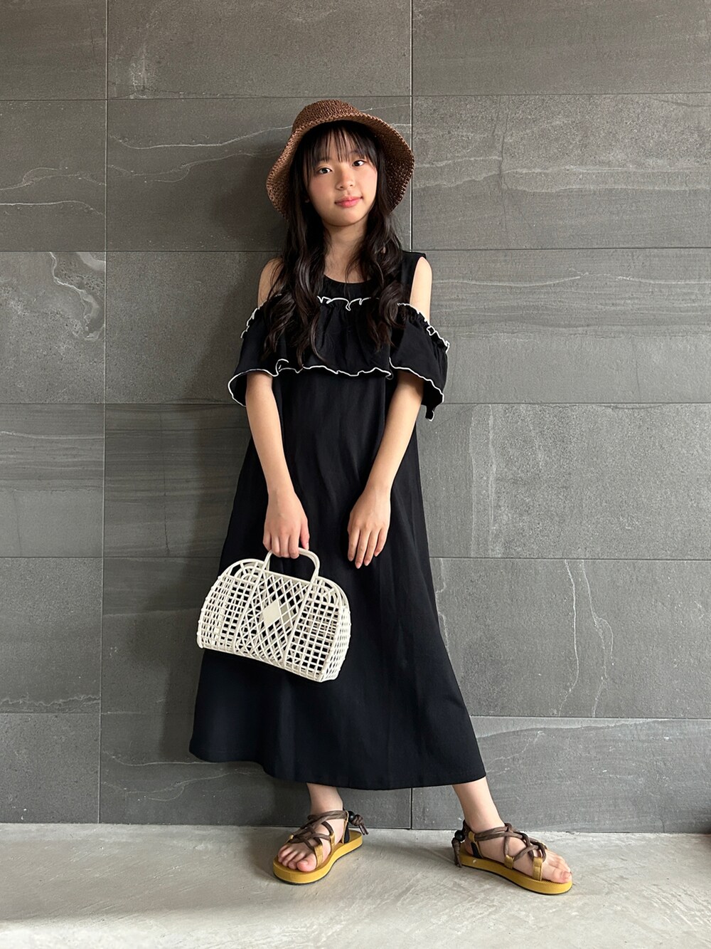 ブラック系のワンピース、オレンジ系のサンダル、ブラウン系のハットを着用したキッズの夏コーディネートの2枚目の写真