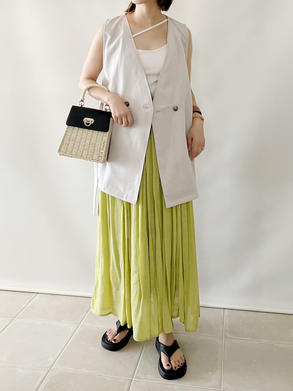 ベージュ系のベスト、ホワイト系のキャミソール、イエロー系のスカートを着用したレディースの夏コーディネートの2枚目の写真