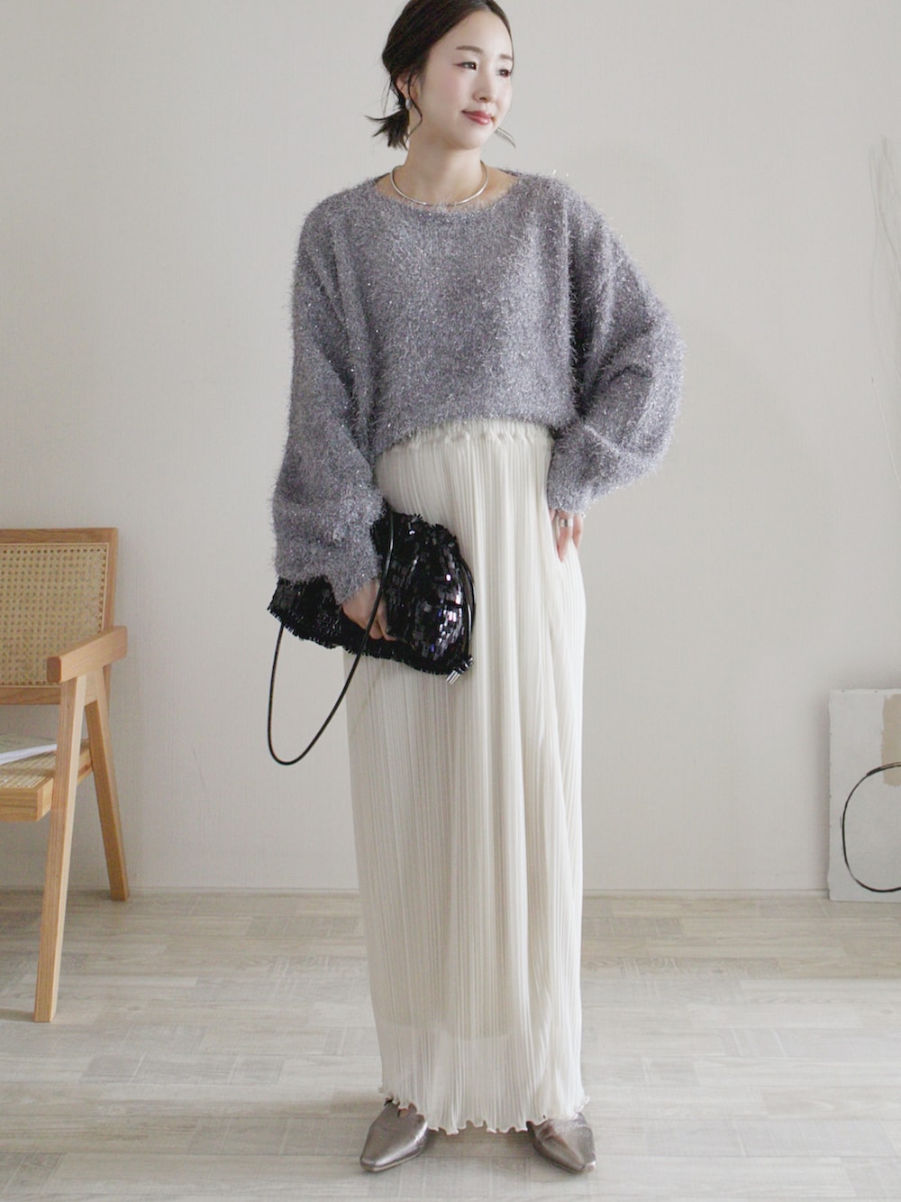 グレー系のニット/セーター、ホワイト系のスカート、ブラック系のクラッチバッグを着用したレディースの秋コーディネートの2枚目の写真