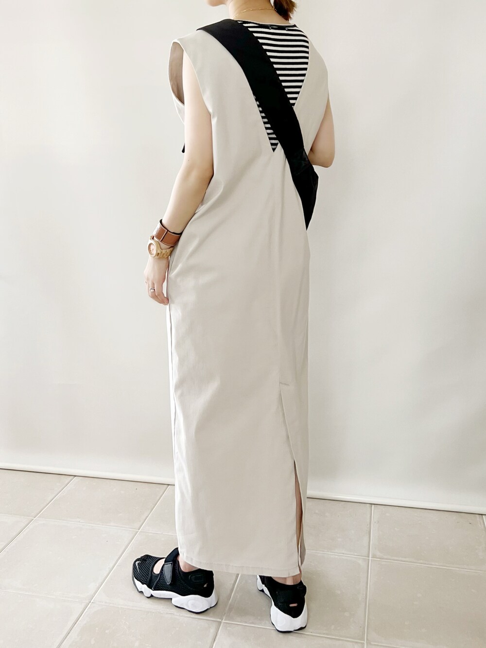 ブラック系のショルダーバッグ、ベージュ系のジャンパースカート、ブラック系のスニーカーを着用したレディースの夏コーディネートの3枚目の写真