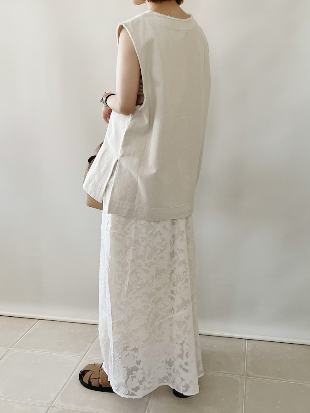 ホワイト系のベスト、ホワイト系のスカート、ベージュ系のバッグを着用したレディースの夏コーディネートの2枚目の写真