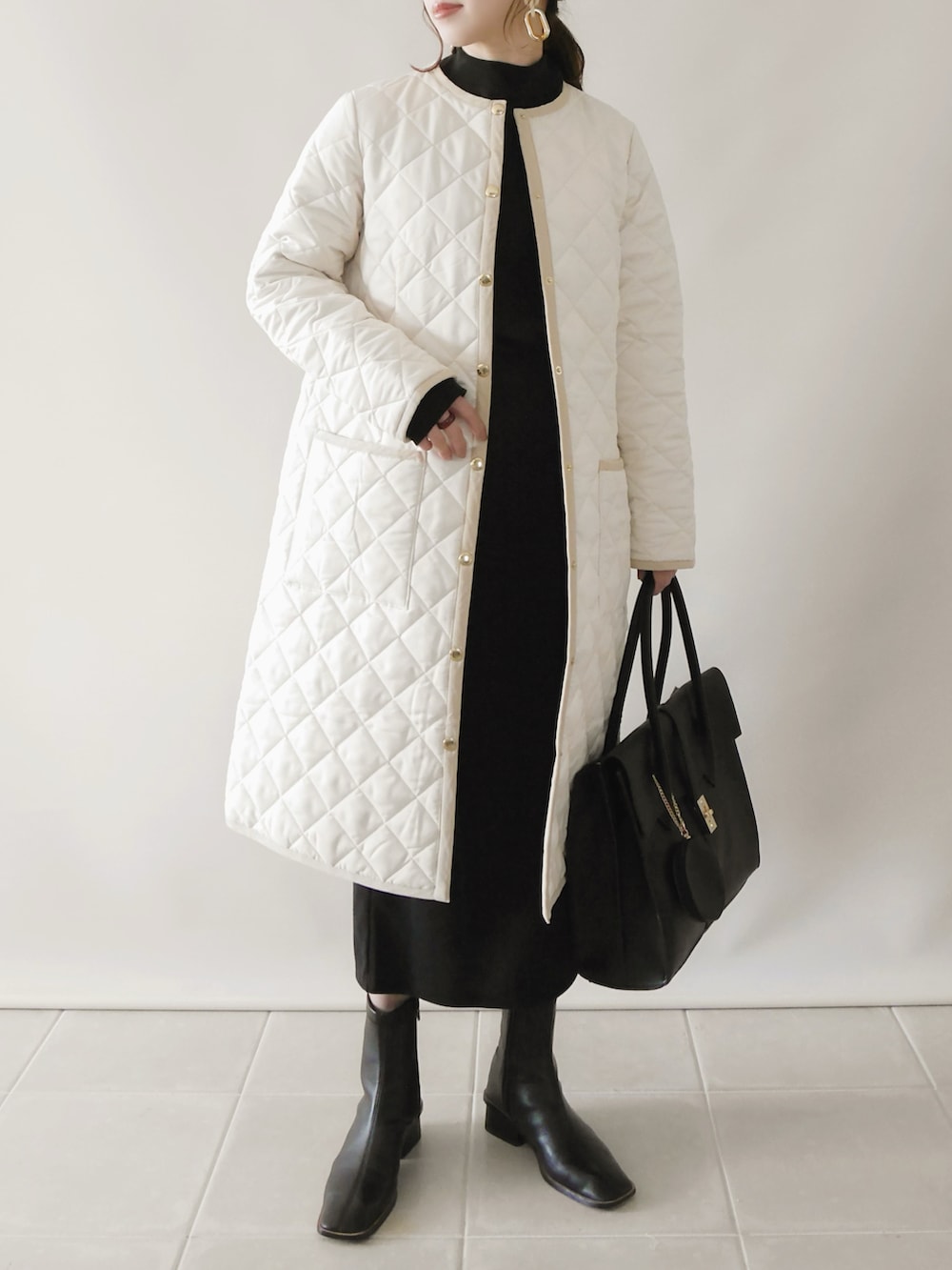 ホワイト系のノーカラーコート、ブラック系のトップス、ブラック系のビジネスバッグを着用したレディースの秋コーディネートの2枚目の写真