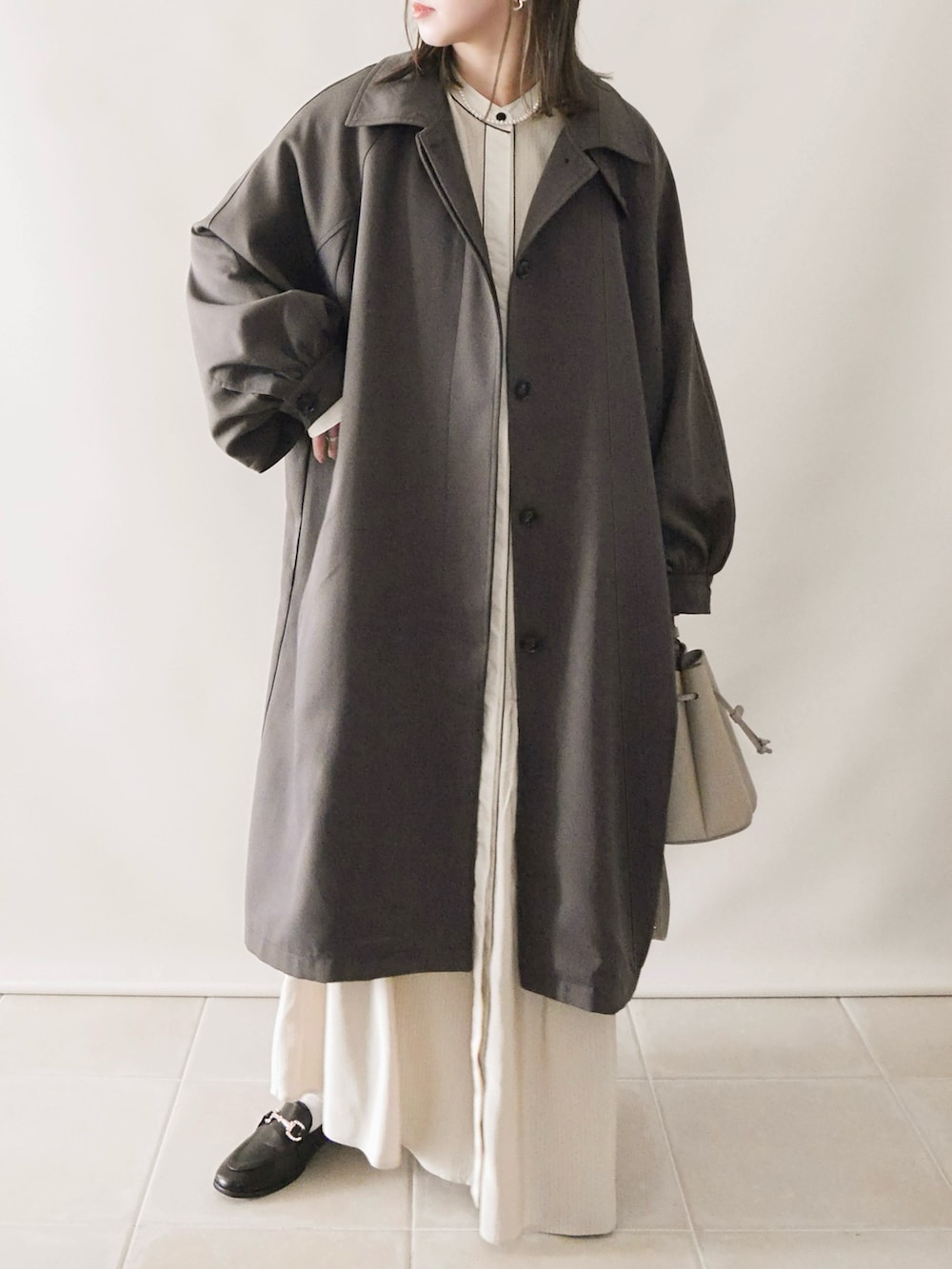 グレー系のステンカラーコート、ホワイト系のワンピース、グレー系のバッグを着用したレディースの冬コーディネートの4枚目の写真