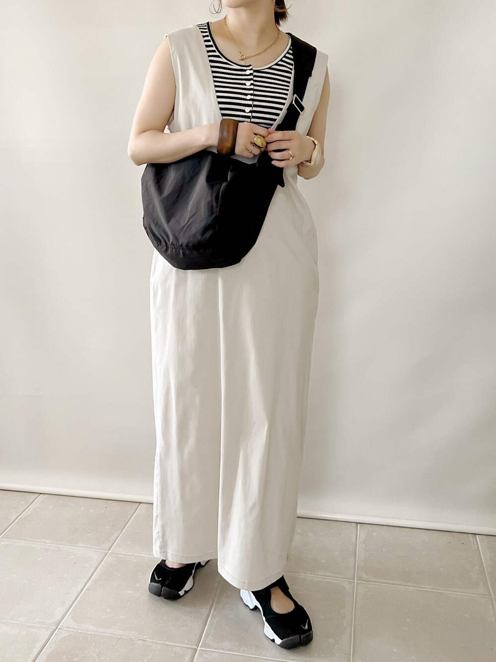 ブラック系のショルダーバッグ、ベージュ系のジャンパースカート、ブラック系のスニーカーを着用したレディースの夏コーディネートの2枚目の写真