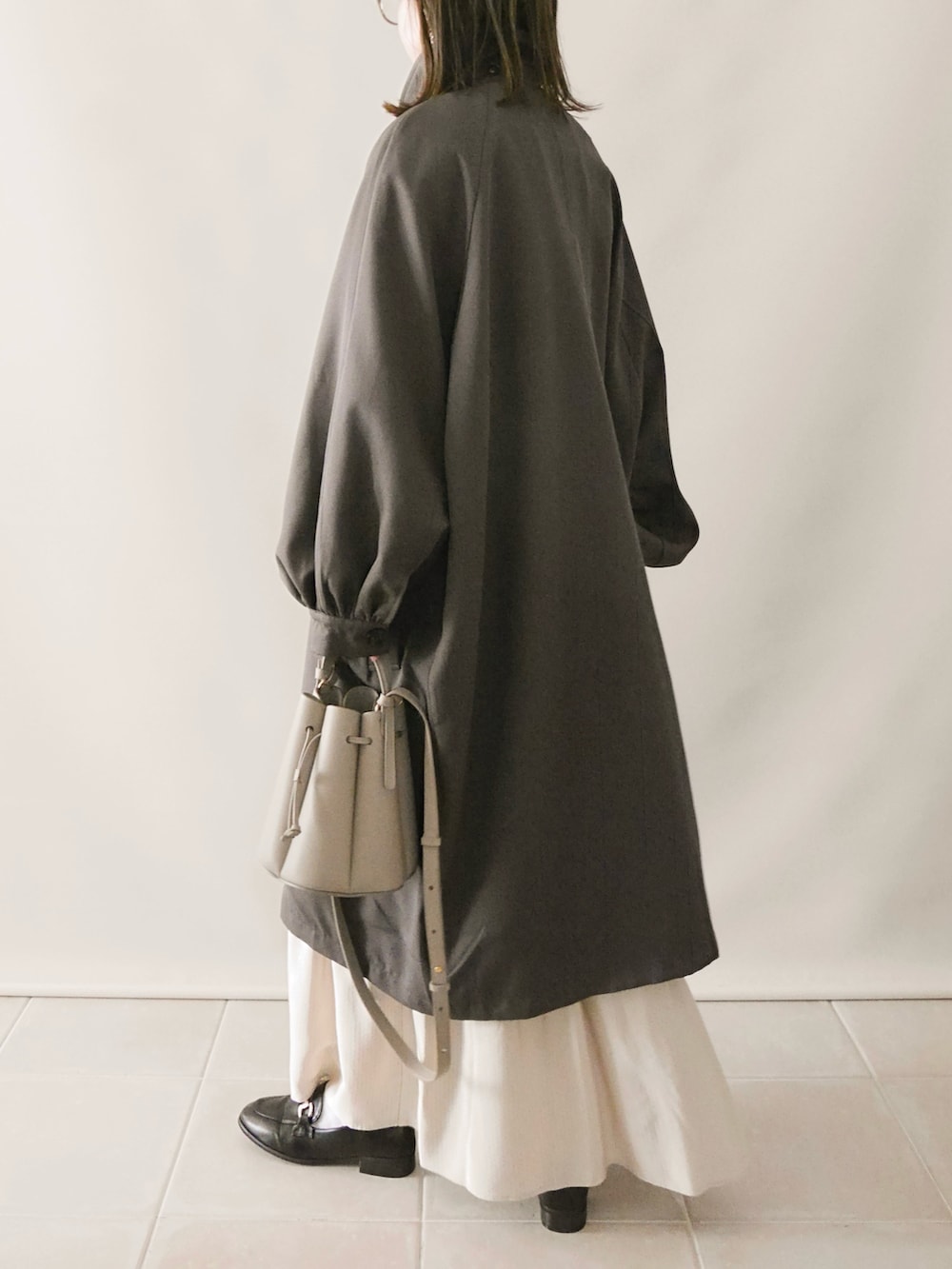 グレー系のステンカラーコート、ホワイト系のワンピース、グレー系のバッグを着用したレディースの冬コーディネートの5枚目の写真