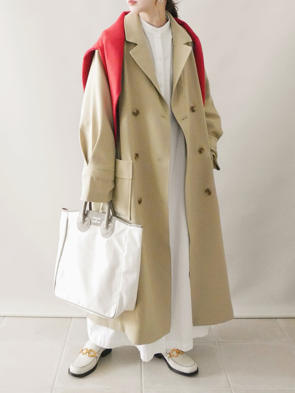 ベージュ系のトレンチコート、ホワイト系のシャツワンピース、ベージュ系のトートバッグを着用したレディースの冬コーディネートの2枚目の写真