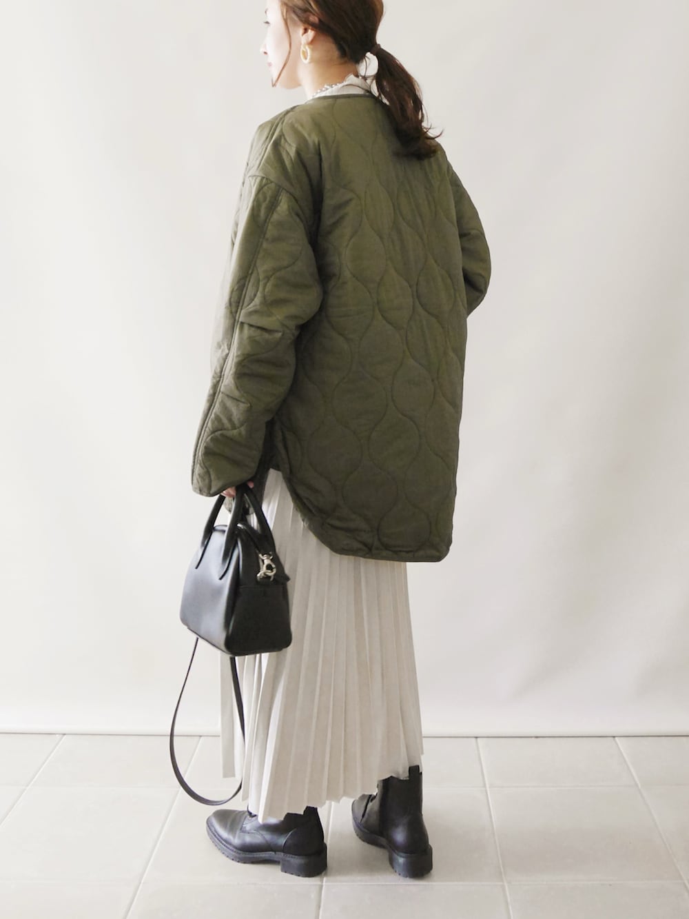 グリーン系のノーカラーコート、ブラック系のワンピース/ドレス、イエロー系のトートバッグを着用したレディースの秋コーディネートの4枚目の写真