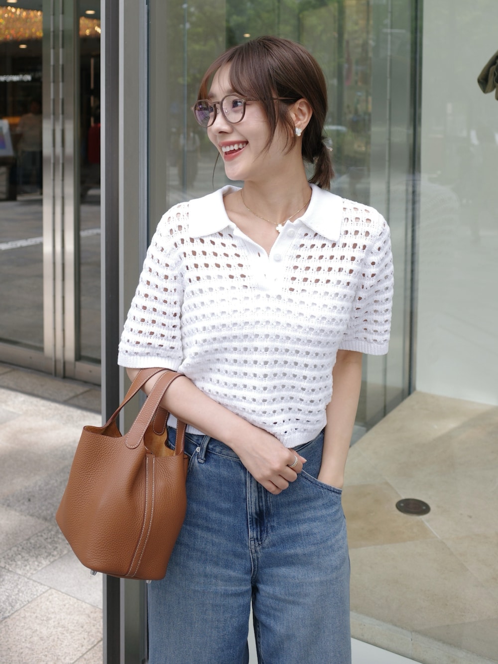 ホワイト系のトップス、ブルー系のデニムパンツ、ブラウン系のハンドバッグを着用したレディースの春コーディネートの2枚目の写真