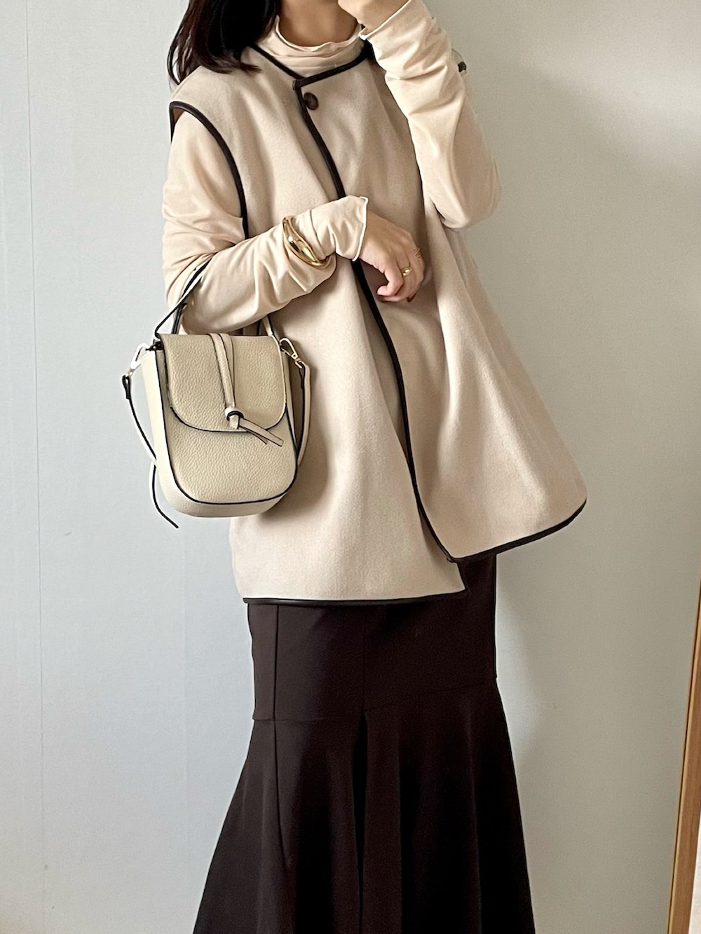 ホワイト系のベスト、ブラウン系のスカート、ホワイト系のショルダーバッグを着用したレディースの秋コーディネートの3枚目の写真