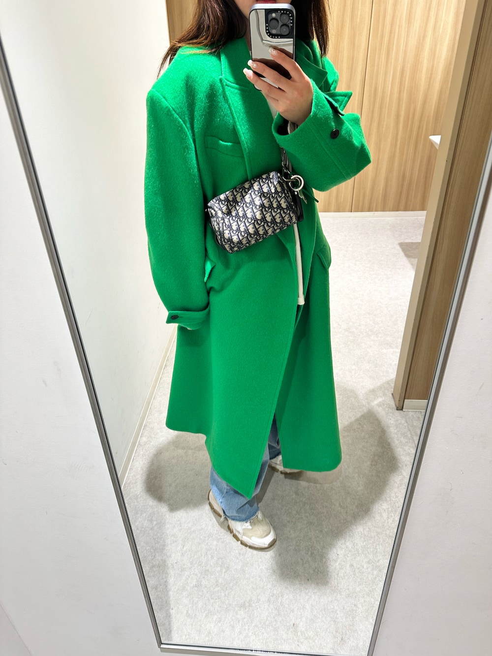 グリーン系のチェスターコート、ブラック系のショルダーバッグ、ホワイト系のスニーカーを着用したレディースの春コーディネートの2枚目の写真