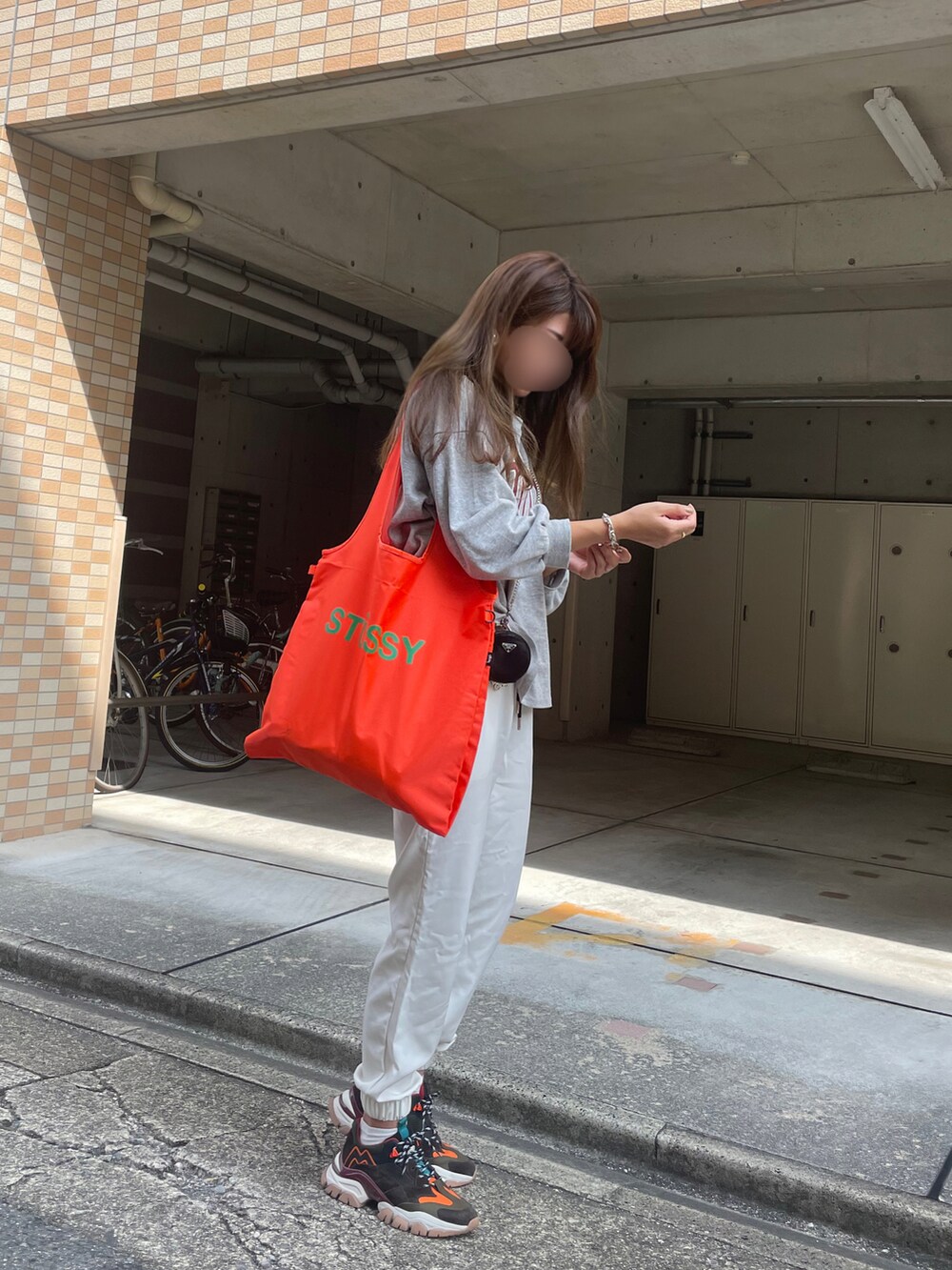 オレンジ系のエコバッグ/サブバッグ、ホワイト系のパンツ、ブラック系のスニーカーを着用したレディースの秋コーディネートの2枚目の写真