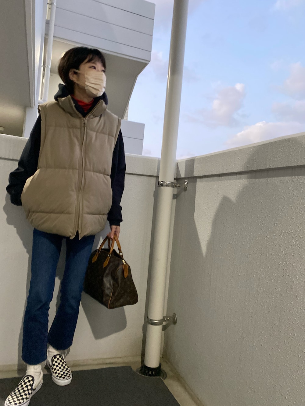 ブラック系のスニーカー、ブルー系のデニムパンツ、ベージュ系のダウンベストを着用したレディースの冬コーディネートの2枚目の写真