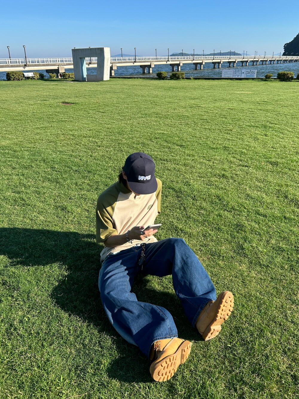 ベージュ系のトップス、ブルー系のデニムパンツ、ベージュ系のブーツを着用したメンズの夏コーディネートの3枚目の写真