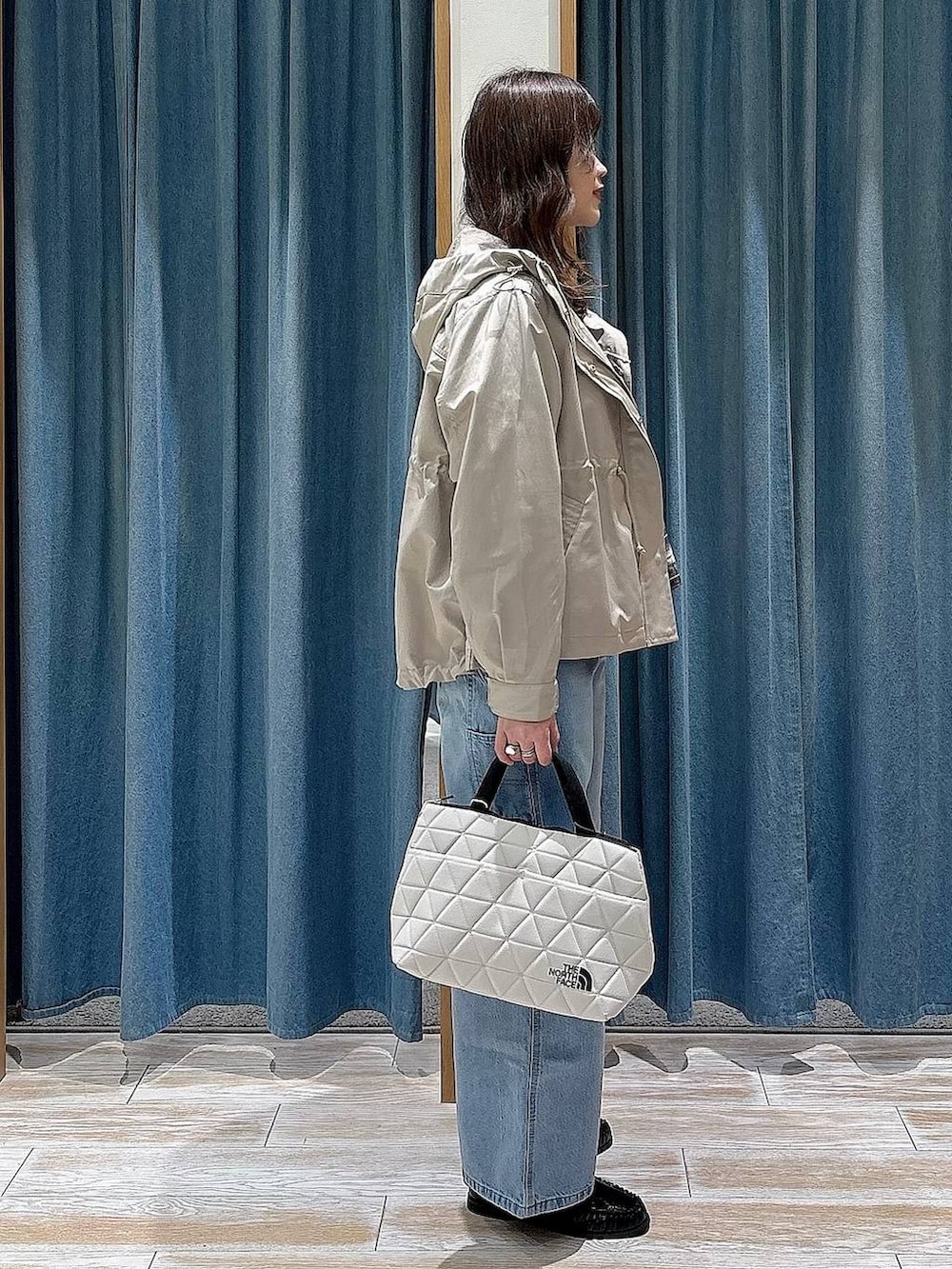 ベージュ系のトートバッグ、ベージュ系のマウンテンパーカー、ブルー系のデニムパンツを着用したレディースの春コーディネートの2枚目の写真