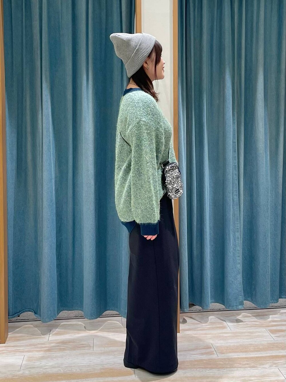 グレー系のショルダーバッグ、ホワイト系のブーツ、グリーン系のニット/セーターを着用したレディースの冬コーディネートの2枚目の写真