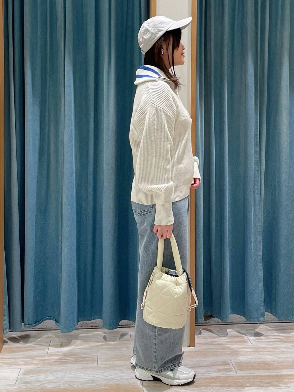 ブルー系のデニムパンツ、ベージュ系のショルダーバッグ、ホワイト系のスニーカーを着用したレディースの冬コーディネートの2枚目の写真