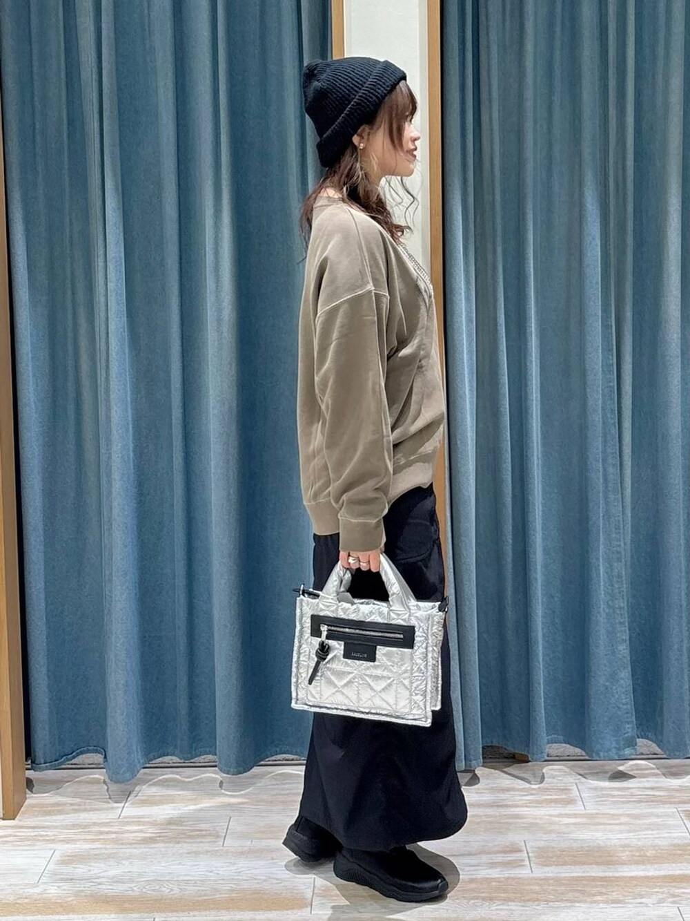 シルバー系のショルダーバッグ、ブラック系のスカート、ブラック系のブーツを着用したレディースの秋コーディネートの2枚目の写真