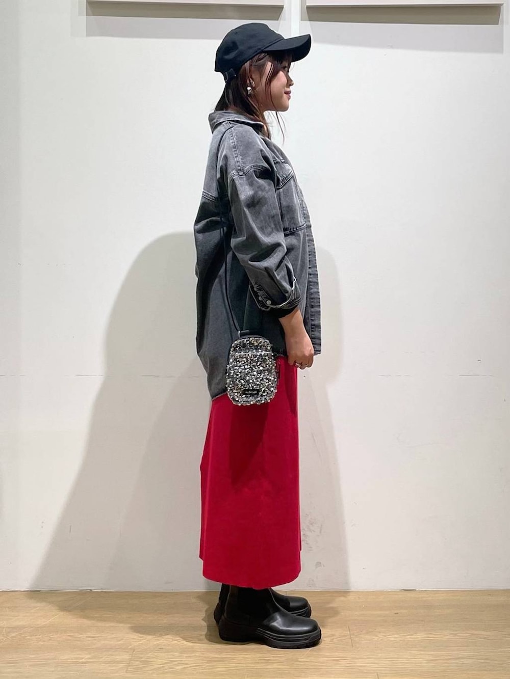 グレー系のショルダーバッグ、レッド系のスカート、ブラック系のブーツを着用したレディースの秋コーディネートの2枚目の写真