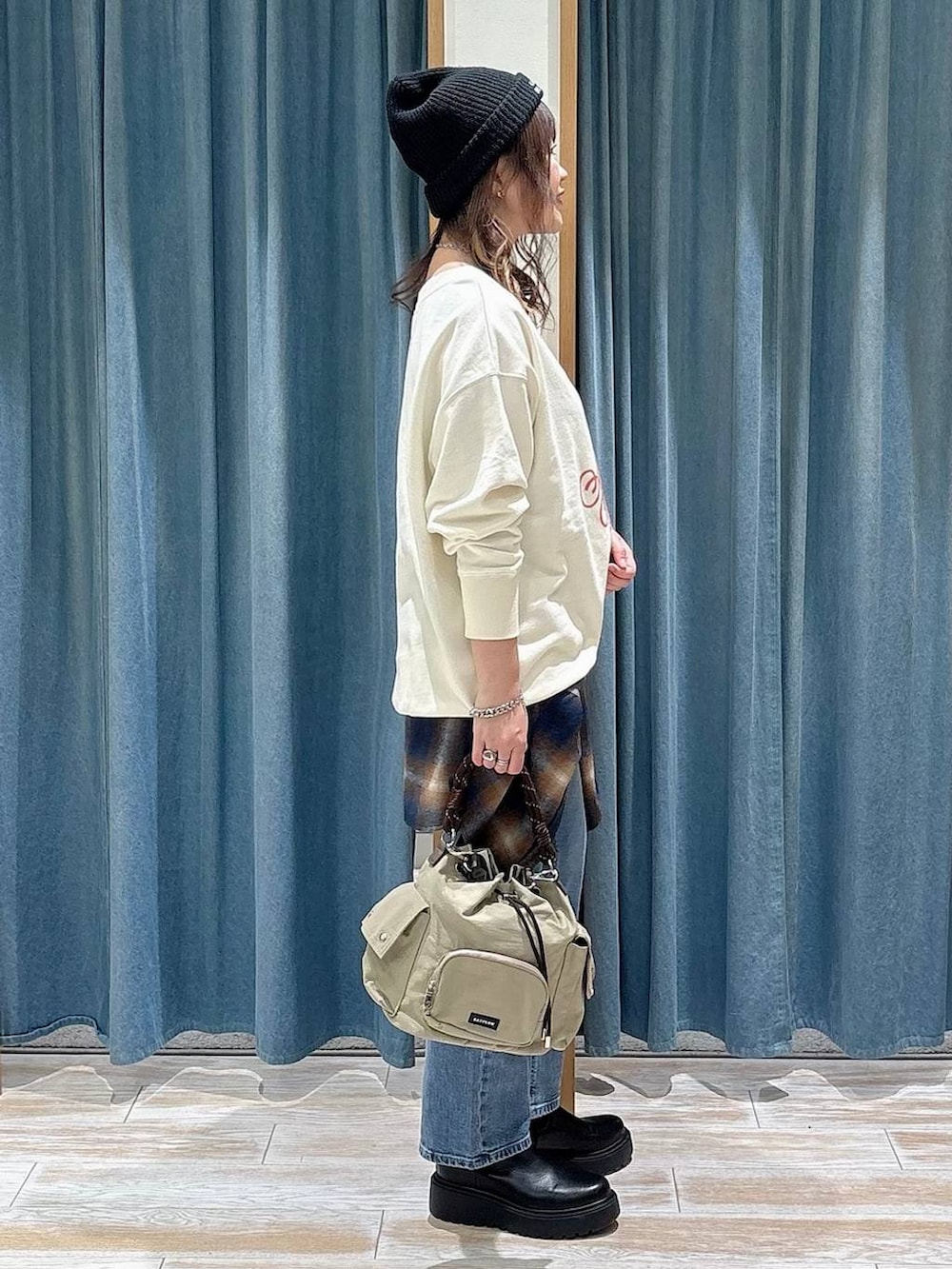 ブラック系のブーツ、ベージュ系のハンドバッグ、ブルー系のデニムパンツを着用したレディースの冬コーディネートの2枚目の写真