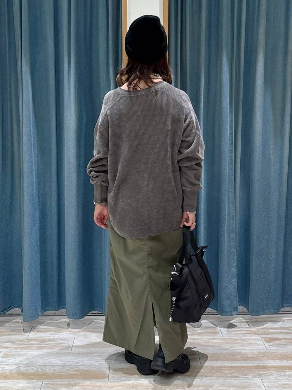 グリーン系のスカート、ブラック系のブーツ、ブラック系のトートバッグを着用したレディースの秋コーディネートの3枚目の写真