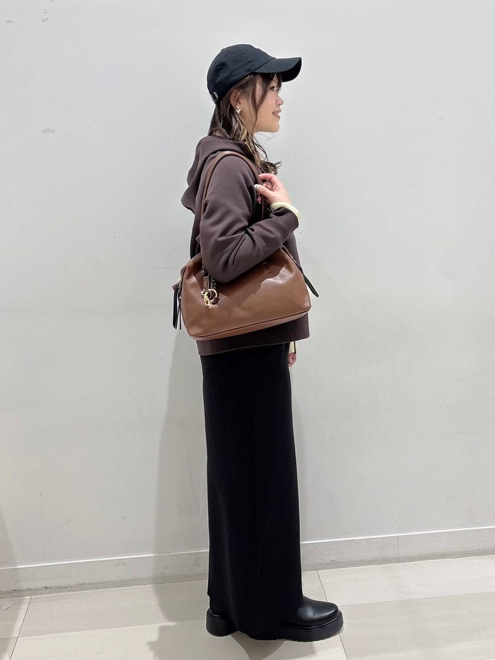 ブラウン系のボストンバッグ、ブラック系のブーツ、ブラウン系のパーカーを着用したレディースの冬コーディネートの2枚目の写真