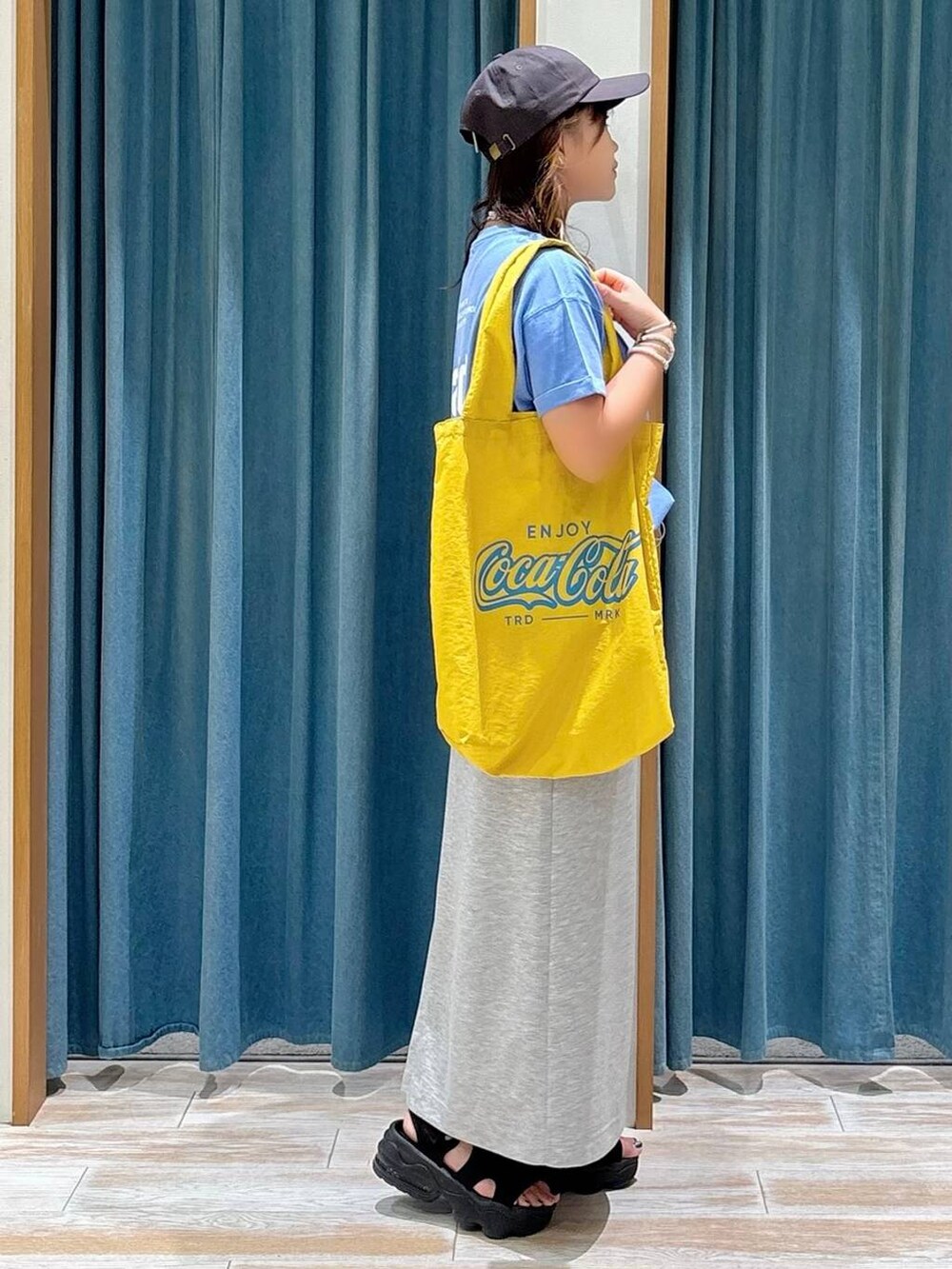 ブルー系のTシャツ/カットソー、イエロー系のトートバッグ、グレー系のスカートを着用したレディースの夏コーディネートの2枚目の写真