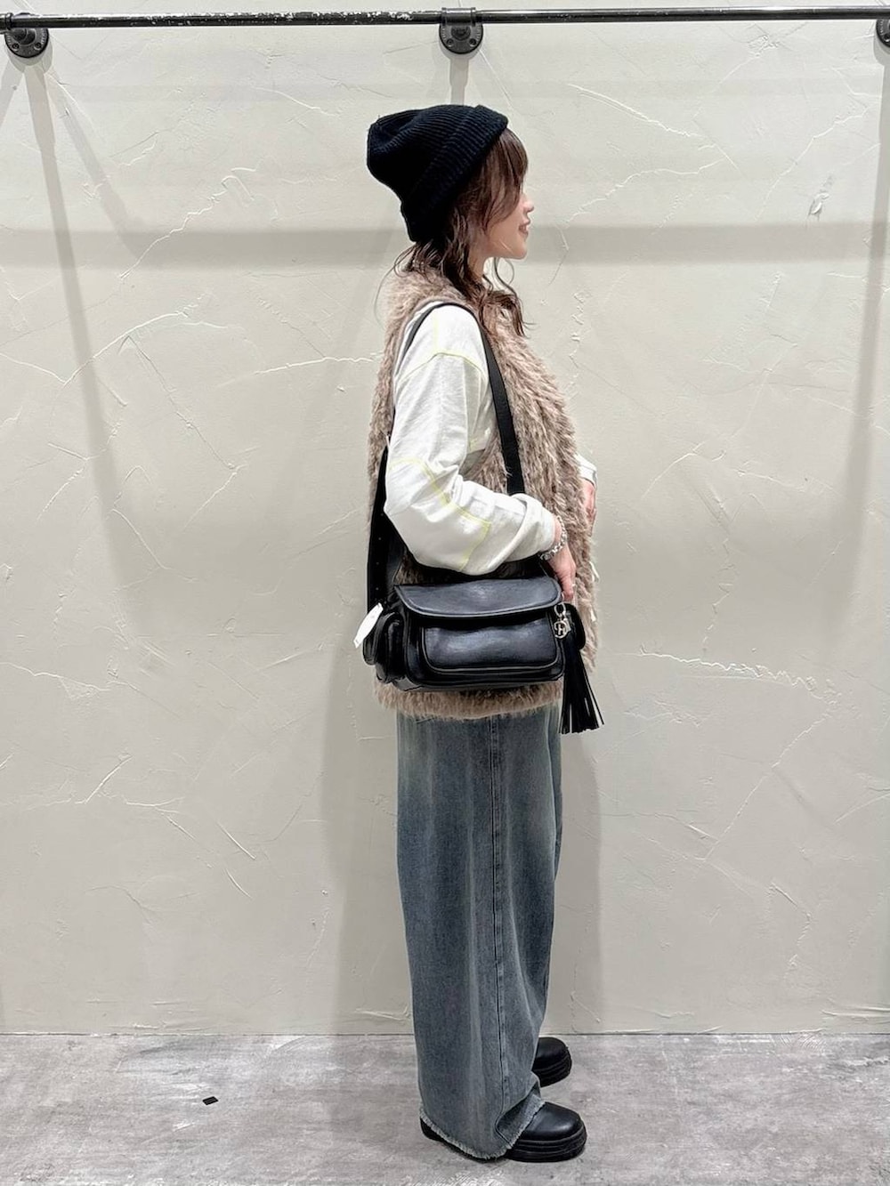 ベージュ系のベスト、ブルー系のデニムパンツ、ブラック系のショルダーバッグを着用したレディースの秋コーディネートの2枚目の写真