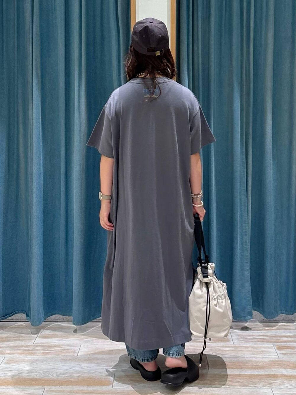 ホワイト系のトートバッグ、ブルー系のデニムパンツ、グレー系のワンピースを着用したレディースの夏コーディネートの3枚目の写真