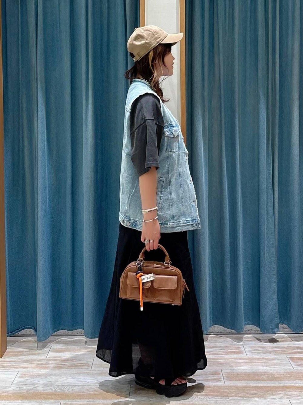 ブラック系のスカート、ブルー系のベスト、ブラウン系のボストンバッグを着用したレディースの夏コーディネートの2枚目の写真