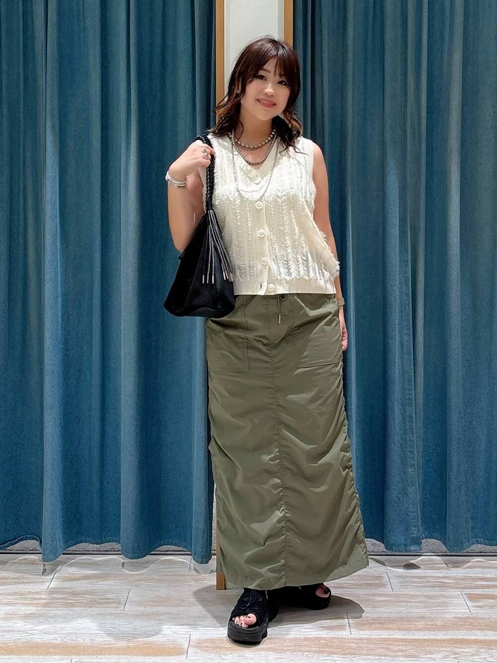 ホワイト系のキャミソール、ブラック系のハンドバッグ、グリーン系のスカートを着用したレディースの夏コーディネートの3枚目の写真