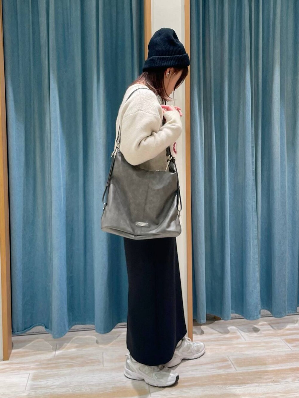 グレー系のショルダーバッグ、ホワイト系のニット/セーター、ブラック系のスカートを着用したレディースの冬コーディネートの2枚目の写真