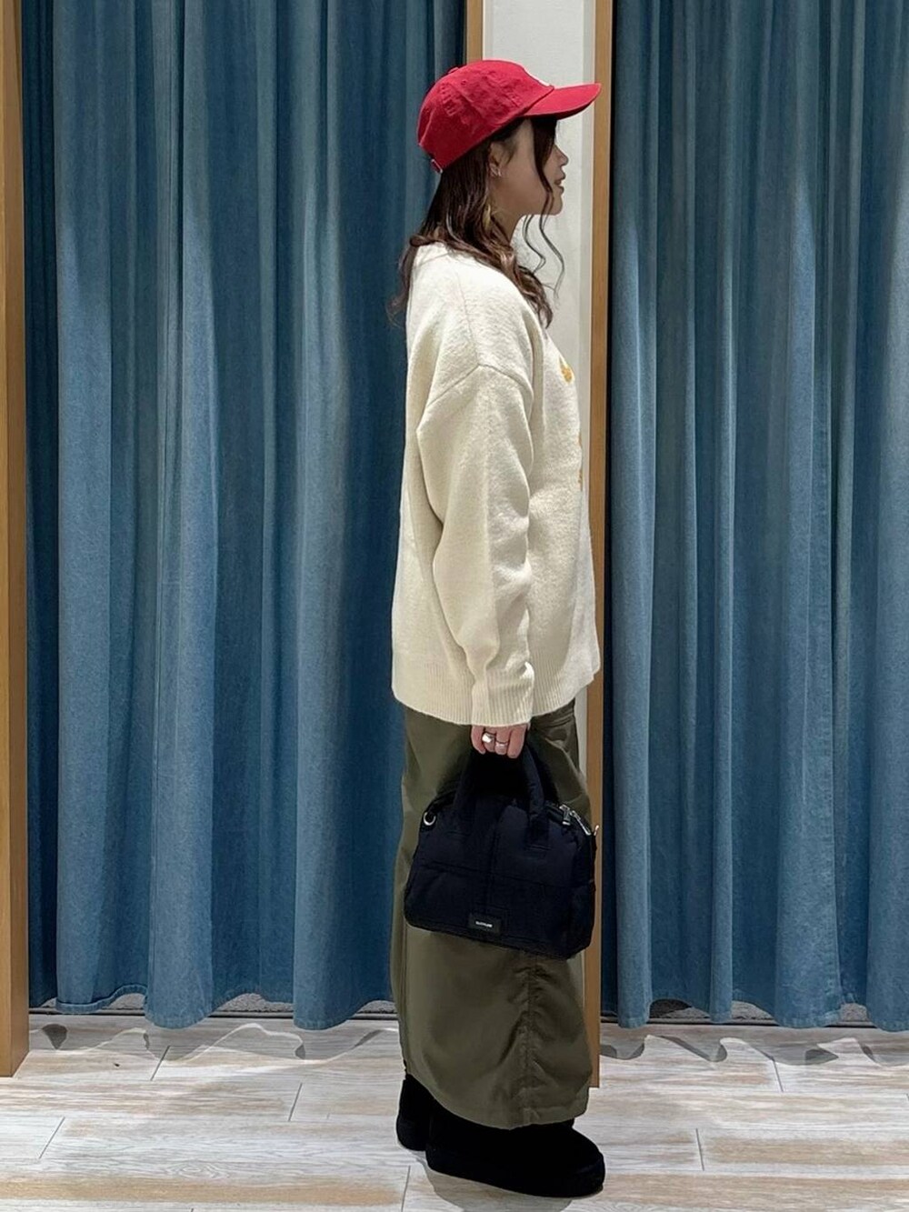 グリーン系のスカート、ブラック系のブーツ、ブラック系のボストンバッグを着用したレディースの秋コーディネートの2枚目の写真