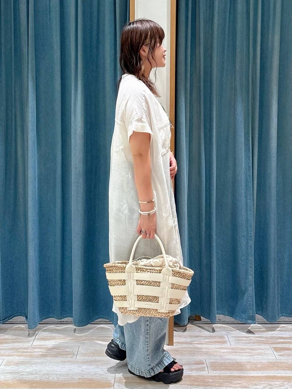ホワイト系のキャミソール、ホワイト系のかごバッグ、ブルー系のデニムパンツを着用したレディースの夏コーディネートの2枚目の写真